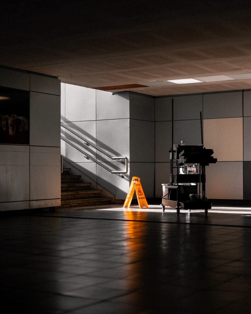 A well-lit underground corridor featuring stairs, cleaning supplies, and warning signs.