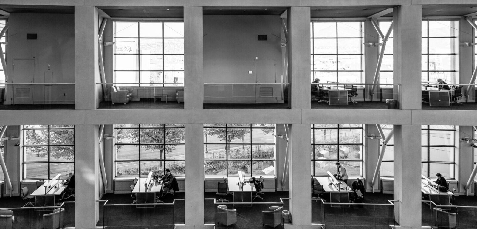 Black and white photo of a modern multi-level office interior with visible workspaces and people.