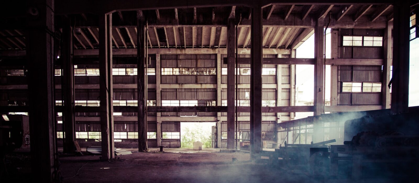A moody interior of a weathered, abandoned warehouse with rusted steel beams and dusty shadows.