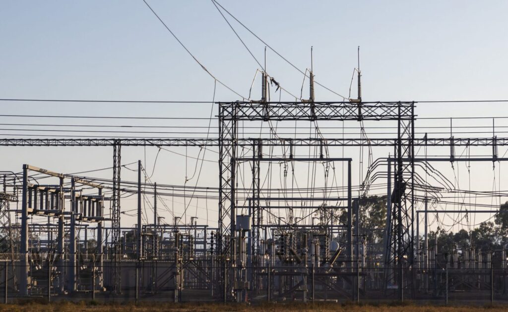 High-voltage electrical substation with steel structures and power lines at dawn.