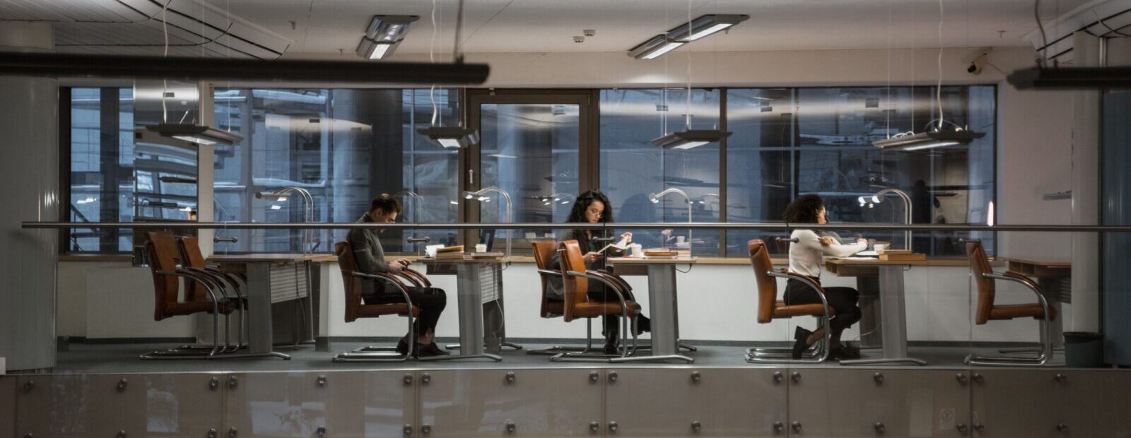 Adults studying in a modern library setting with large windows and ample lighting.